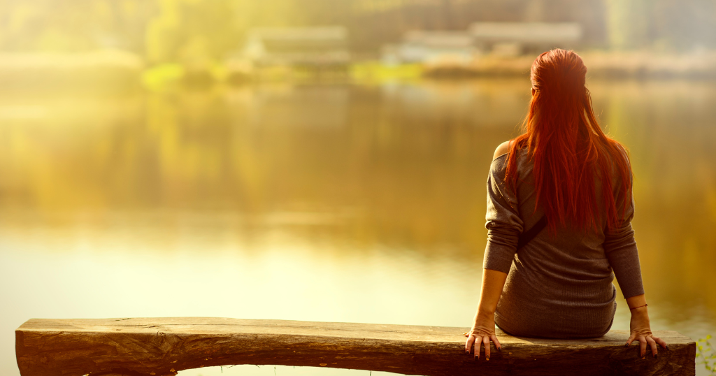 Person sitting by the water at sunset, taking time for reflection and gentle self-care after a tough life moment.