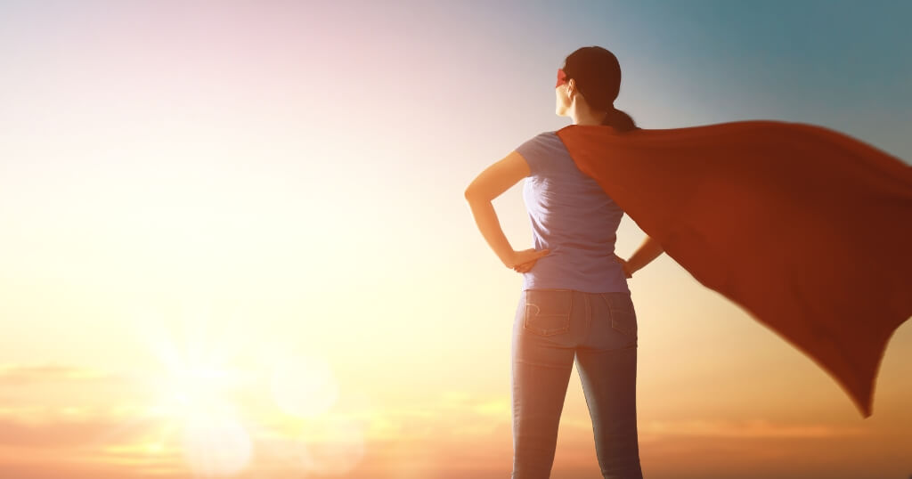 Woman wearing a red superhero cape standing confidently at sunrise, representing confidence, motivation and taking control of her health.