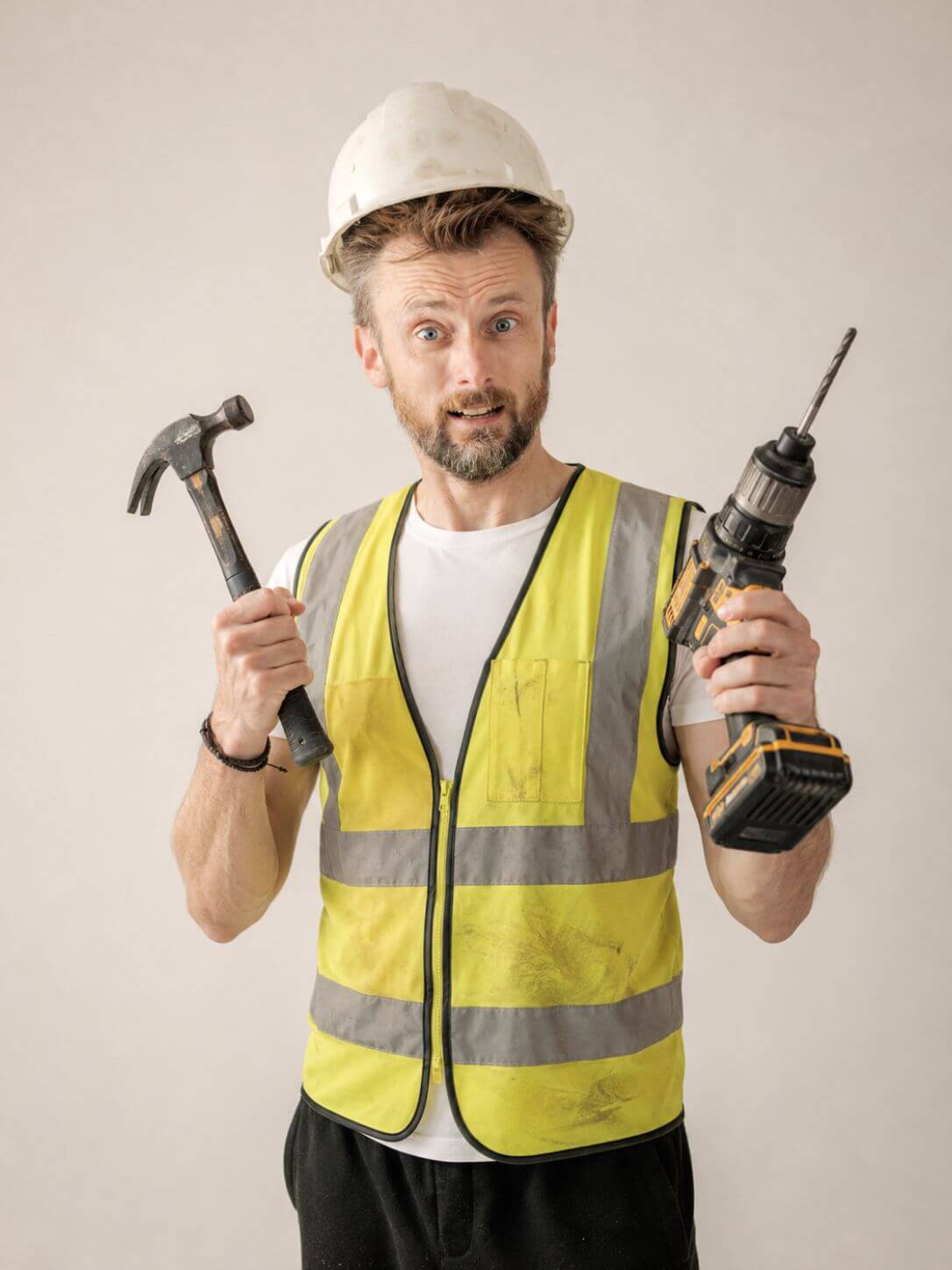 Anthony Punshon holding a hammer and drill while wearing a hard hat and high-visibility vest
